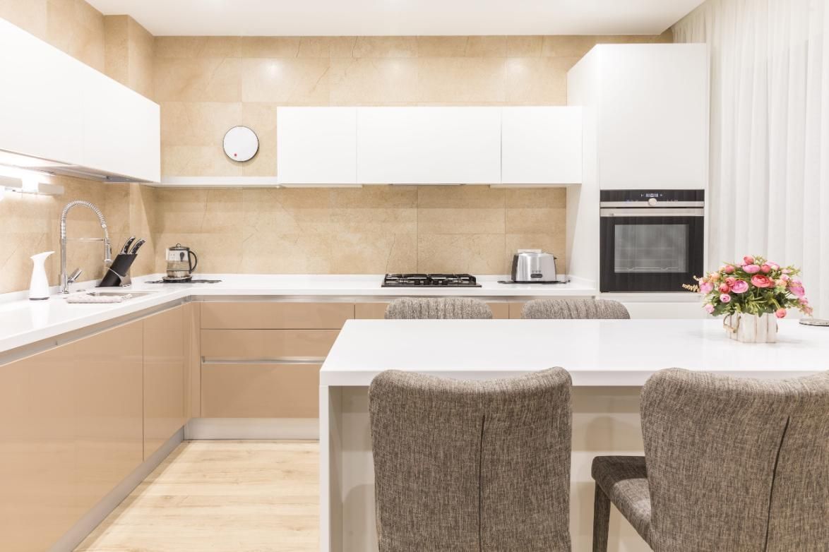 Cocina moderna y luminosa con armarios blancos, salpicadero beige, isla y dos sillas grises.