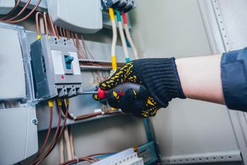 Una mano enguantada ajusta los cables dentro de un panel de control eléctrico.