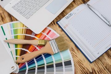 Muestras de color, pinceles, un ordenador portátil y un cuaderno sobre un escritorio