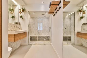 Baño moderno y luminoso con dos lavabos, plantas colgantes y una ducha con mampara de cristal y azulejos de mármol.