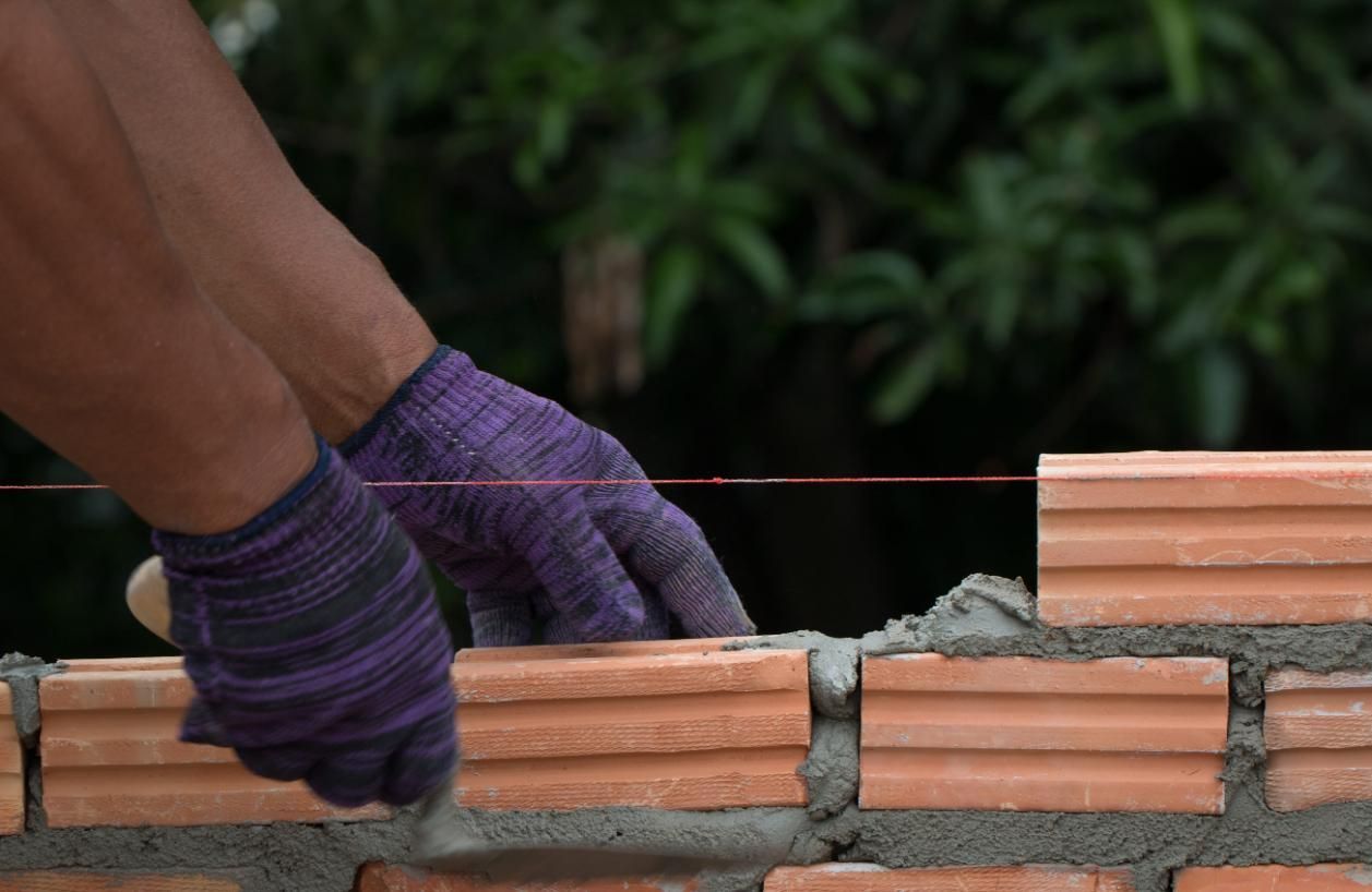 Manos enguantadas colocan ladrillos de terracota con mortero en un muro bajo al aire libre.