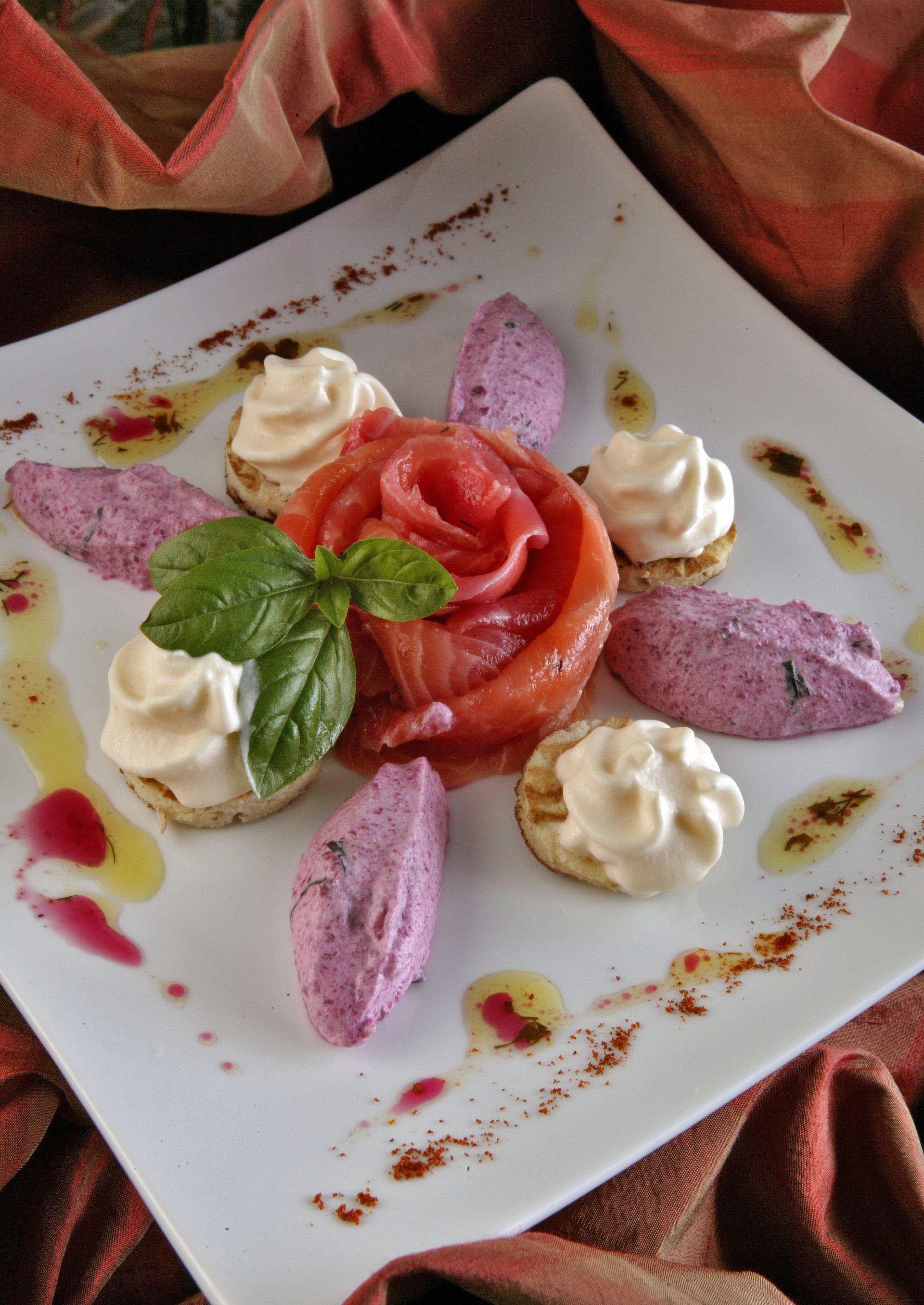 Plat de saumon entouré de portions de crème et de mousse violette, de feuilles de basilic et nappé de sauce