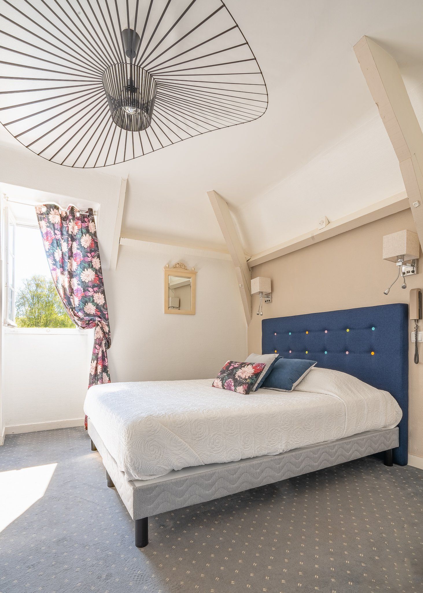 Chambre sous combles avec lit, lumière naturelle et détails fleuris