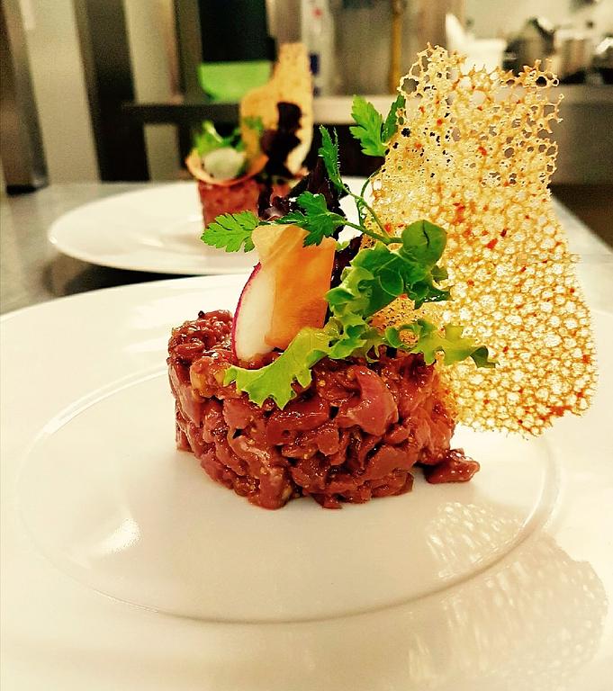 Tartare de viande finement hachée avec une feuille de salade et une décoration croustillante dorée