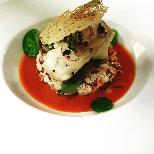 Morceau de poisson blanc avec une sauce rouge sur un lit de légumes accompagné d'herbes et d'une gaufrette