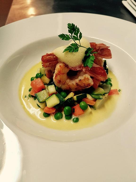 Plat avec des crevettes poêlées sur un lit de légumes en dés dans une sauce jaune et garnis d'herbes