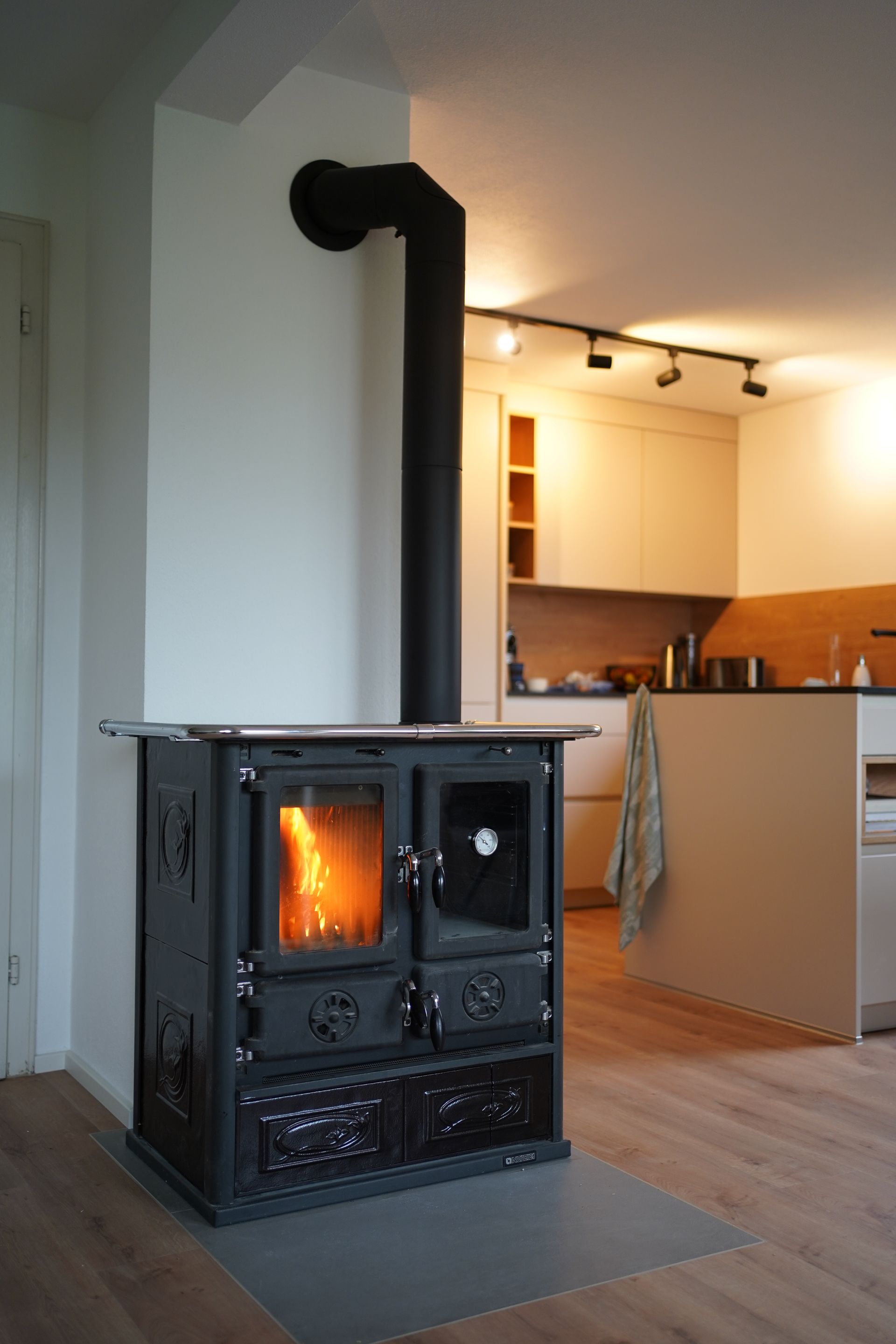 Cuisinière à bois installée dans une cuisine moderne ouverte, avec foyer en fonctionnement.
