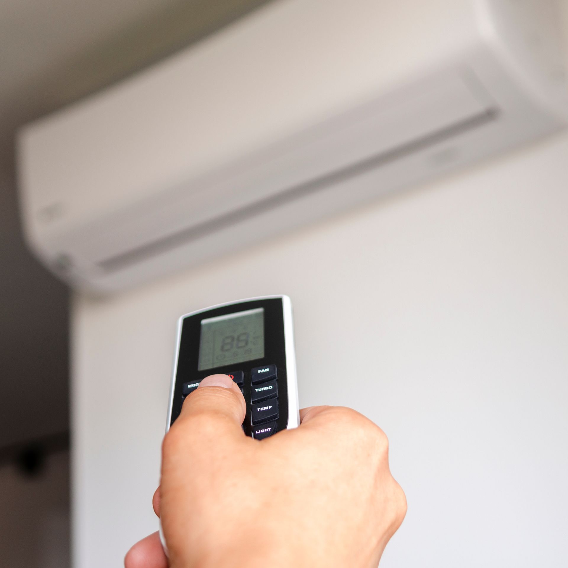 Une personne tient la télécommande d’un climatiseur devant l’unité de climatisation afin de régler la température intérieure.