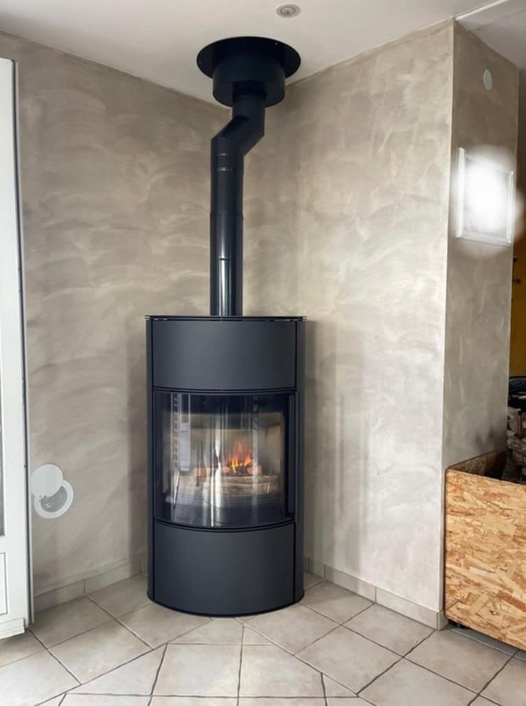 Poêle à bois noir avec flamme visible dans une pièce d'angle carrelée