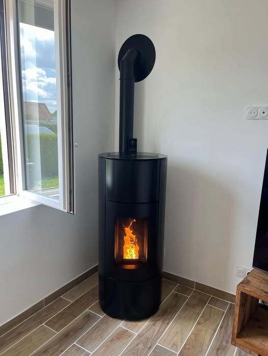 Poêle à bois noir avec un feu crépitant dans un coin de pièce près d'une fenêtre, sur un sol carrelé marron
