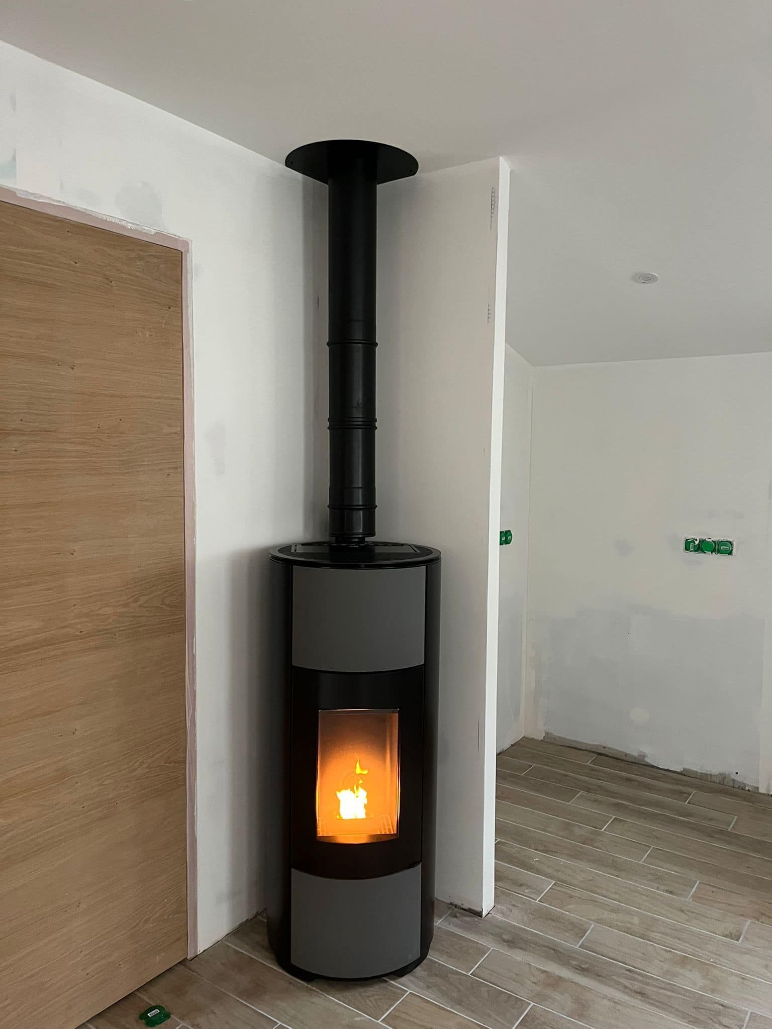Poêle à bois noir avec un feu incandescent dans un coin de pièce claire, à côté d'un store baissé.