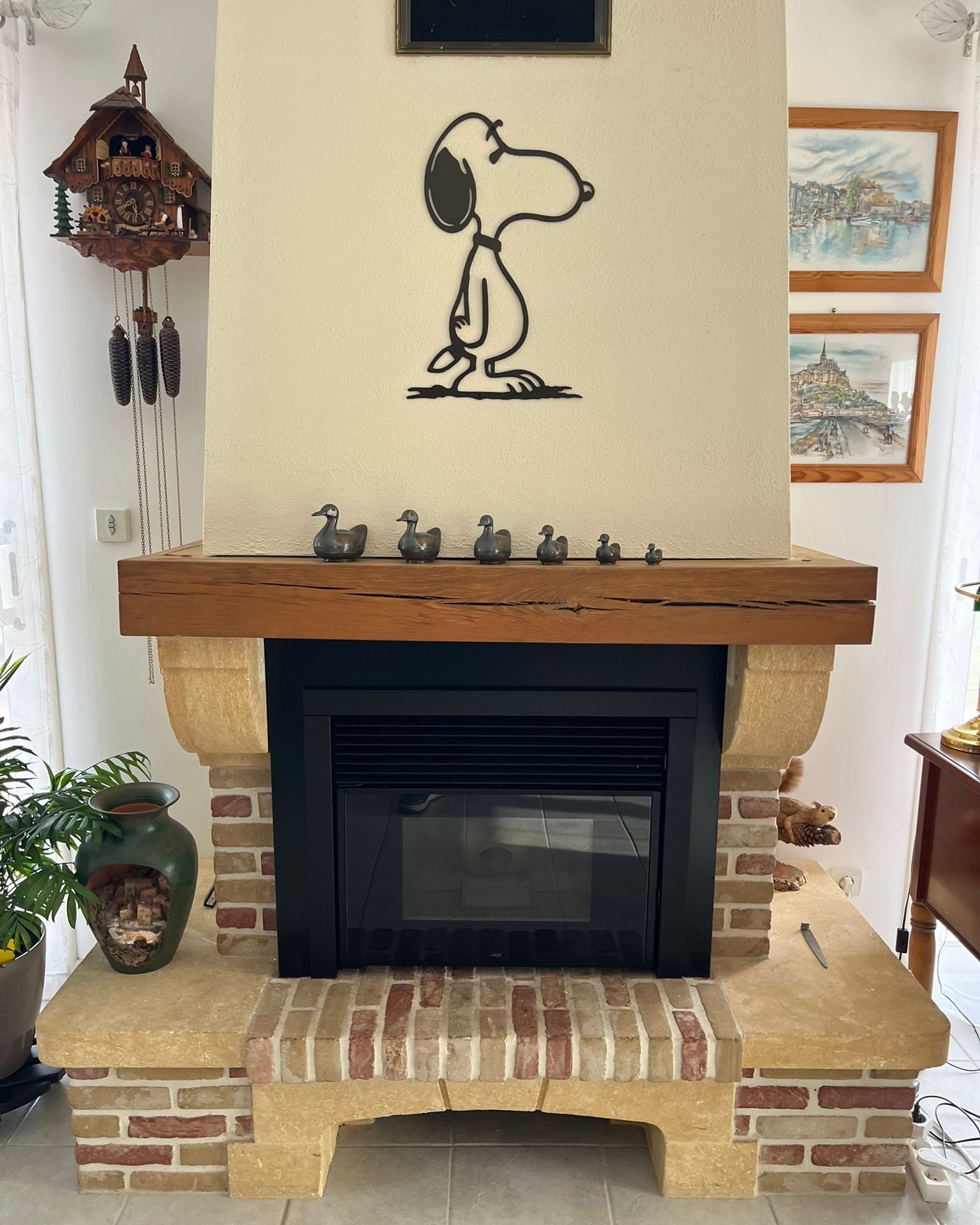 Cheminée du salon avec entourage en briques, manteau en bois, décoration murale Snoopy et petites figurines sur le dessus