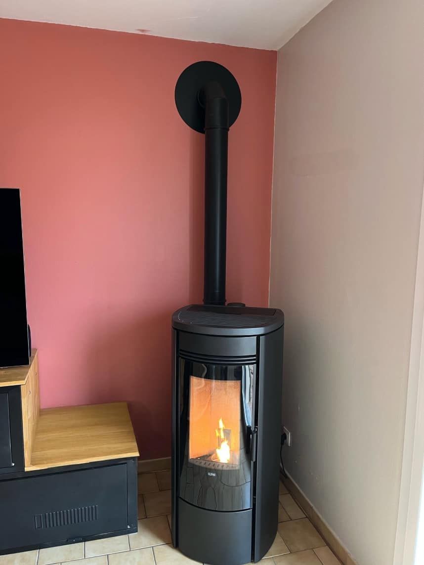 Poêle à bois noir avec des flammes visibles dans un coin, à côté d'un mur rose et d'un mur beige.