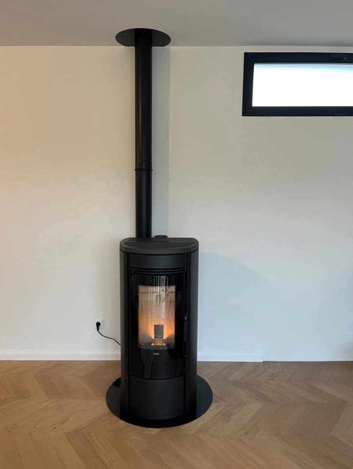 Poêle à bois noir indépendant avec un feu crépitant dans une pièce minimaliste avec parquet clair et petite fenêtre.