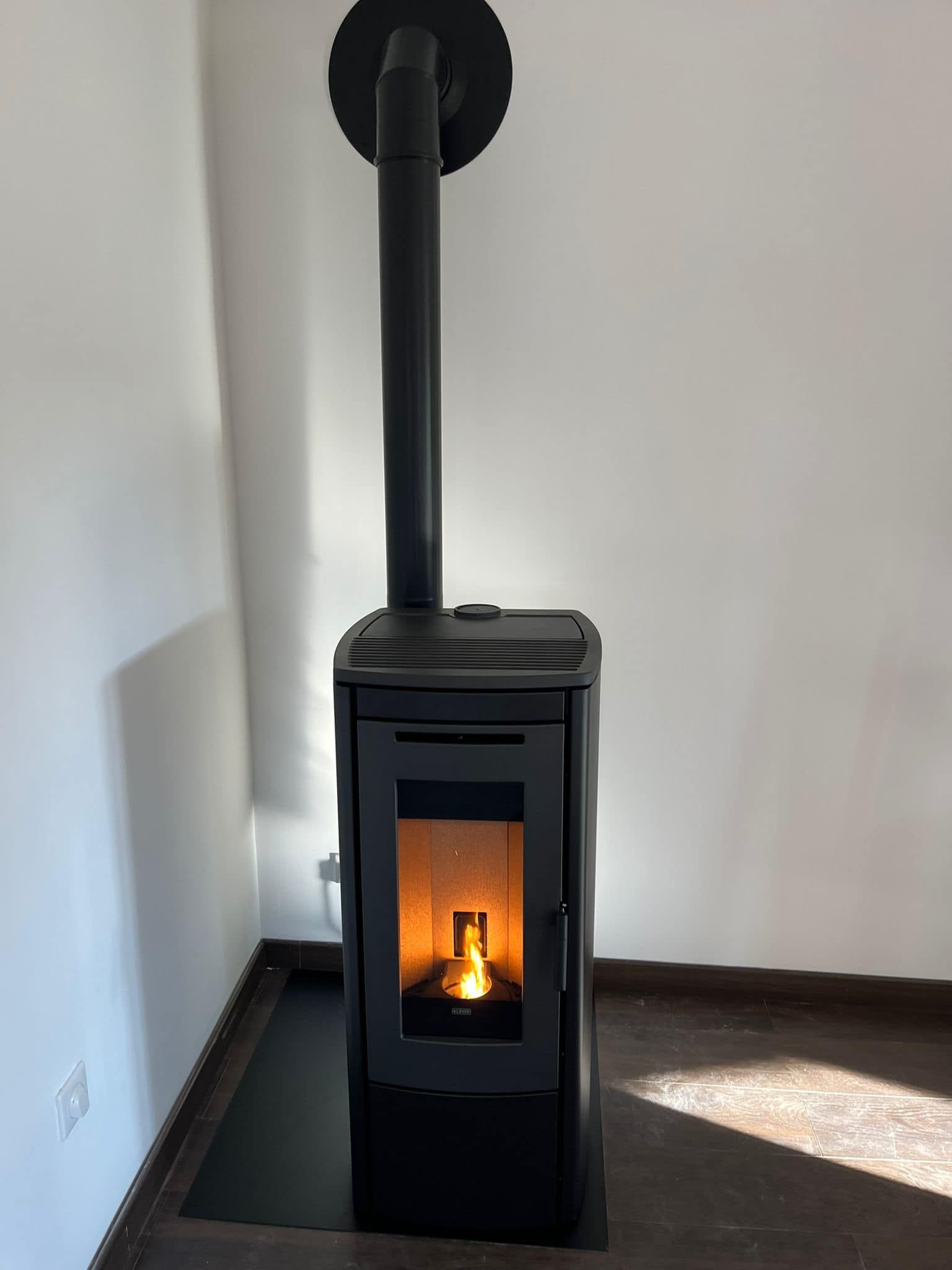 Poêle à granulés noirs avec un feu incandescent et un conduit de cheminée sur un foyer dans un coin de pièce