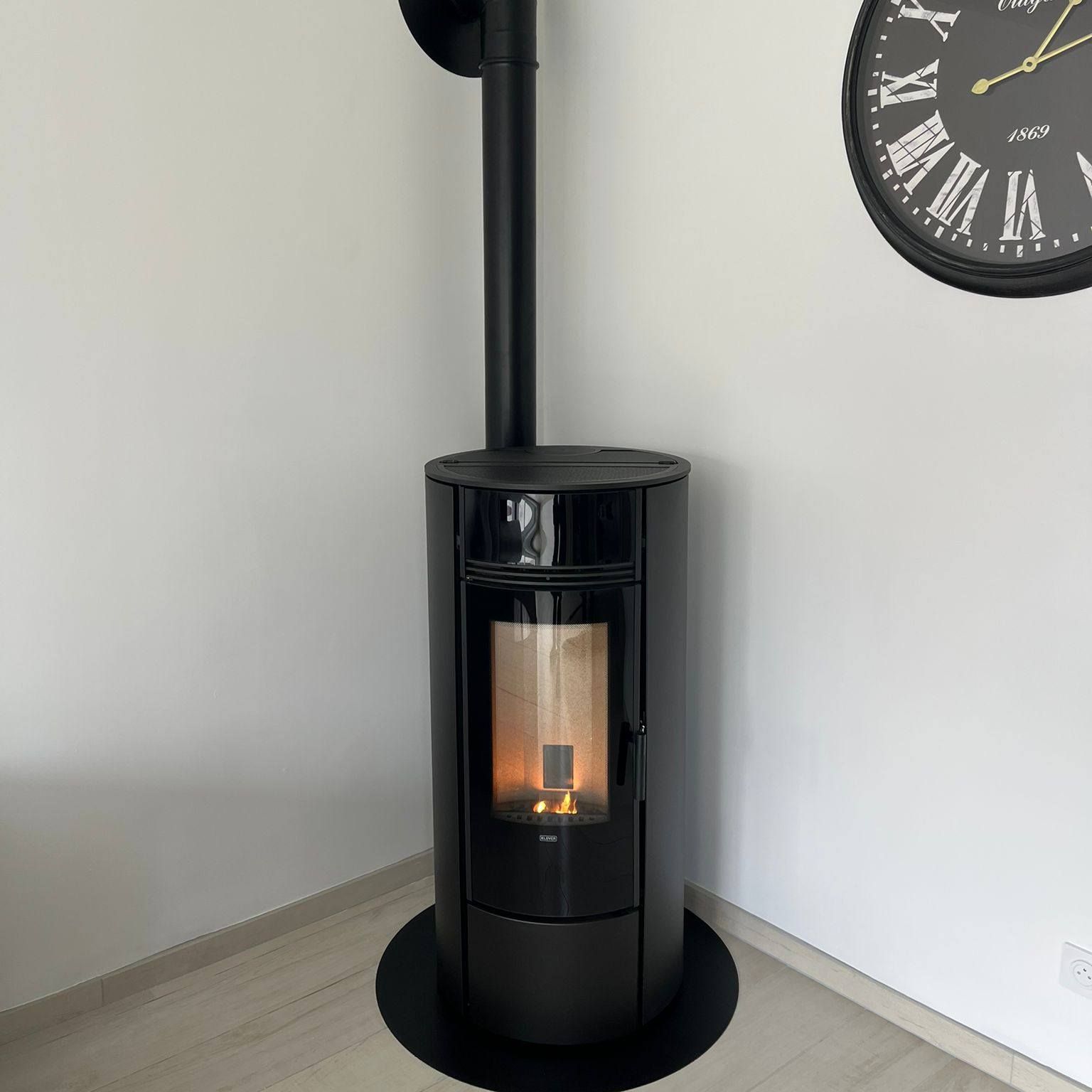 Poêle à bois noir indépendant avec un petit feu dans une pièce d'angle à côté d'une horloge murale