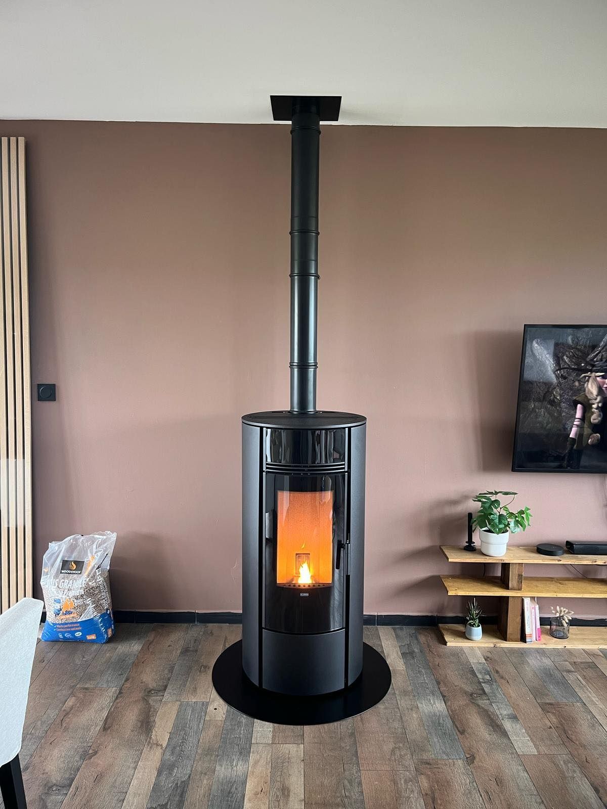 Poêle à bois noir indépendant avec conduit de cheminée dans un salon, flammes incandescentes visibles.