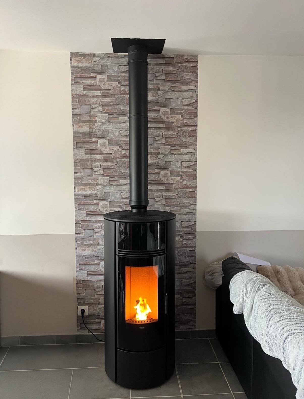 Poêle à bois noir avec un feu allumé sur fond de pierre dans un salon, à côté d'un canapé.