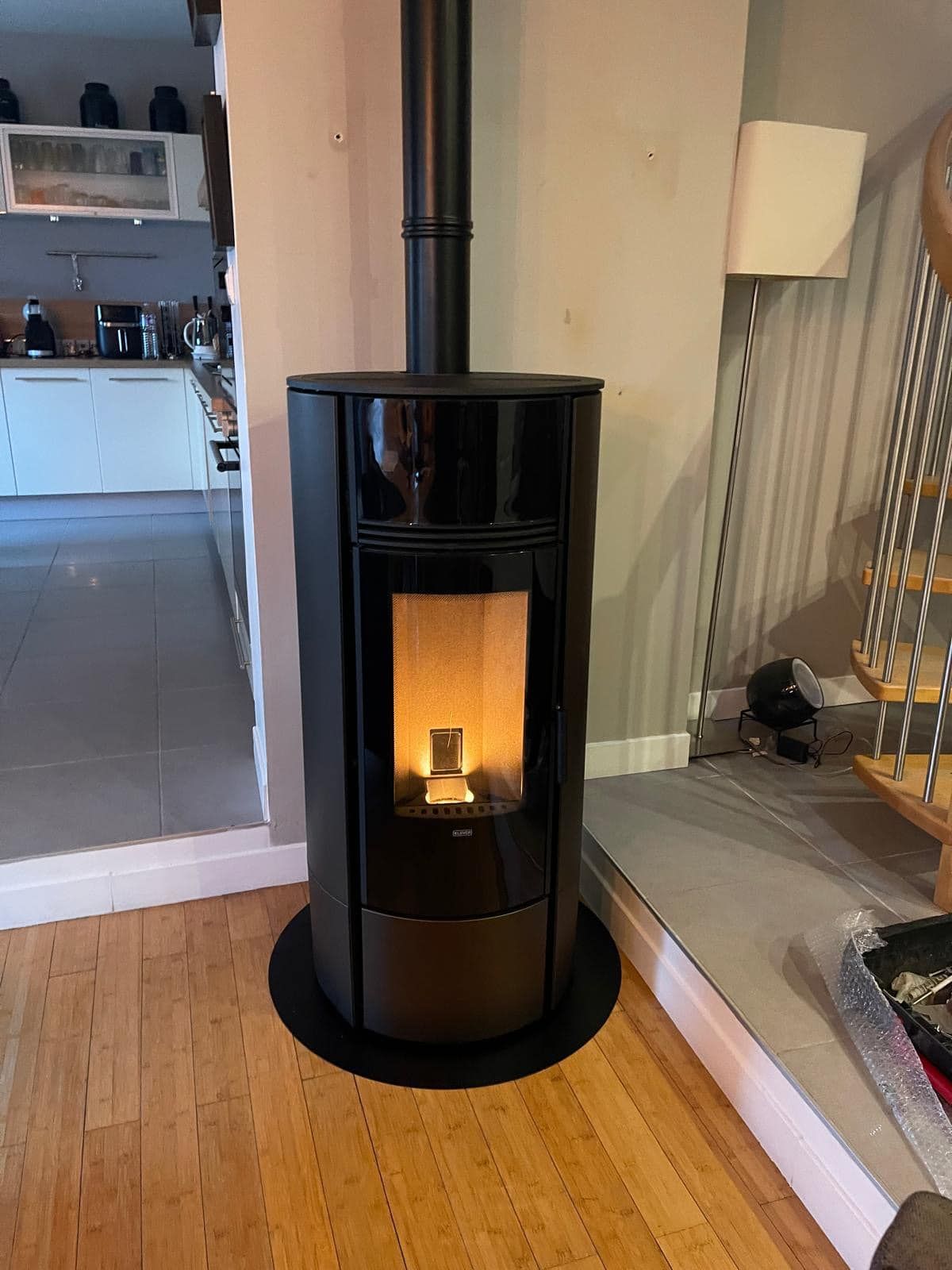 Poêle à granulés cylindrique noir incandescent sur un parquet à l'intérieur d'une maison.