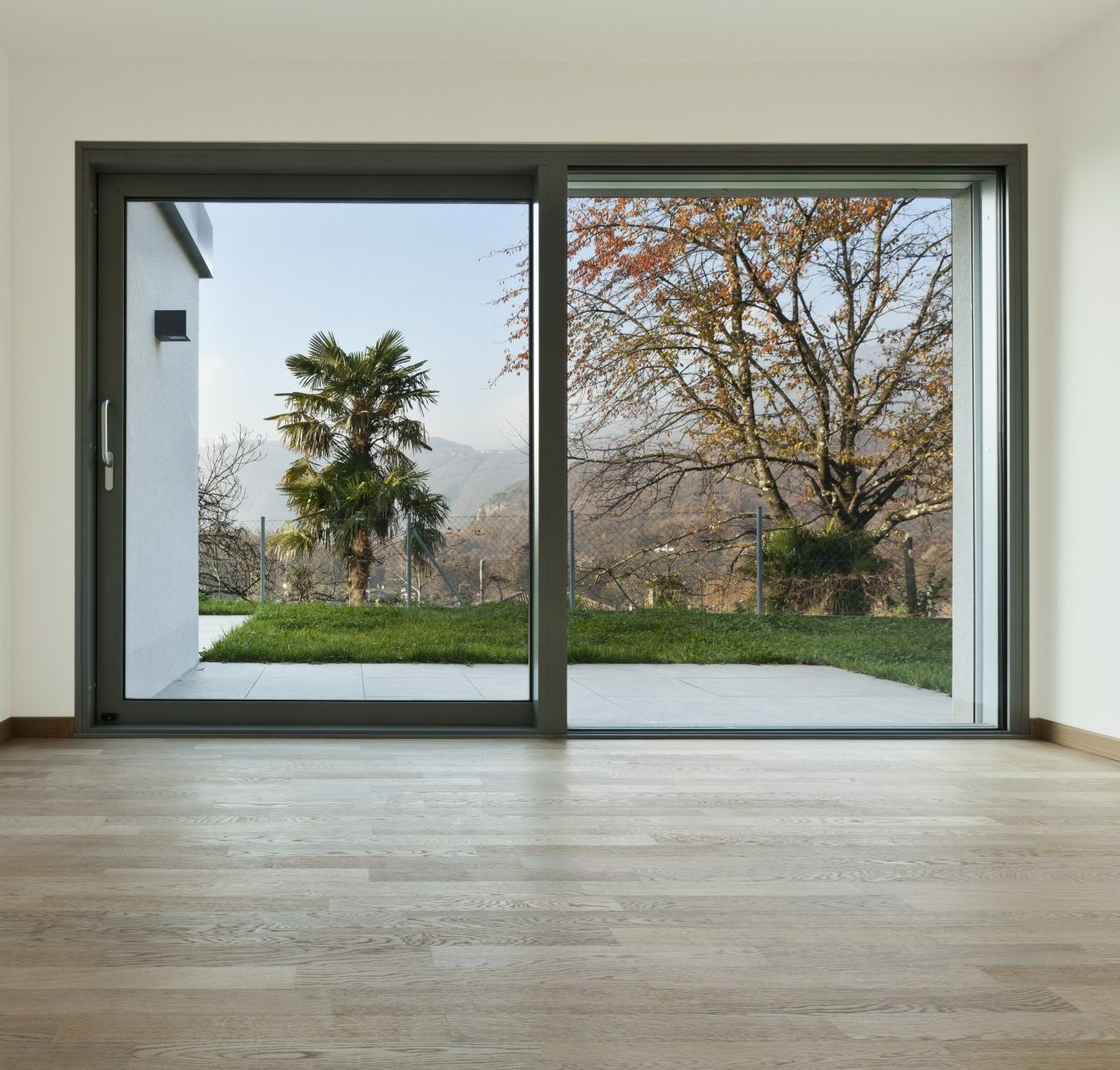 Grande baie vitrée coulissante en aluminium donnant sur un jardin arboré.