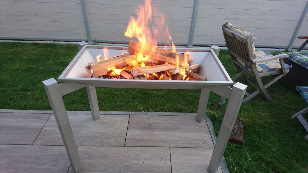 Eine hochgestellte Feuerschale aus Metall mit einem kleinen Feuer auf einer Terrasse