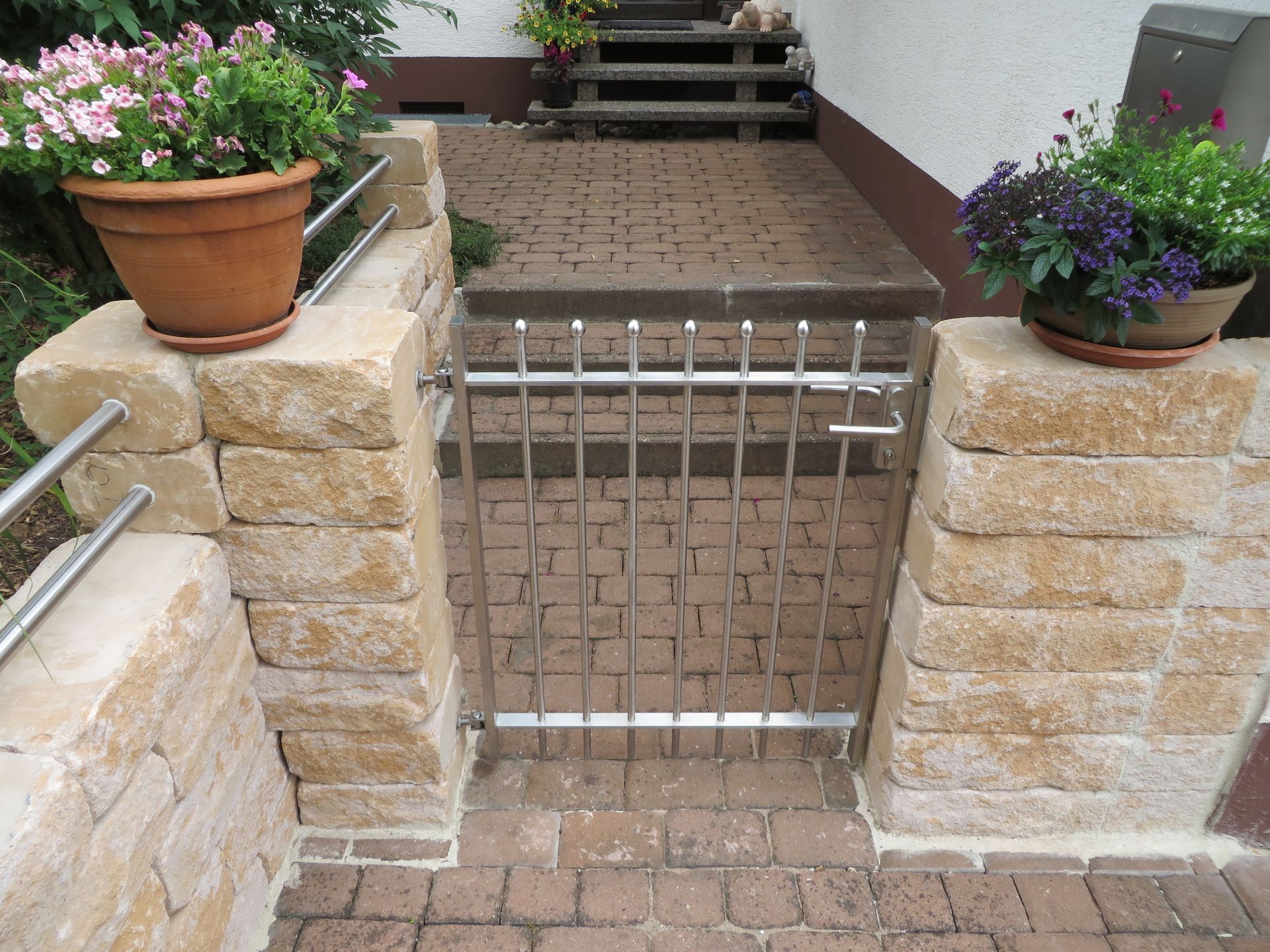 Grundstückszaun aus Naturstein mit Metallstangen und Metalltor