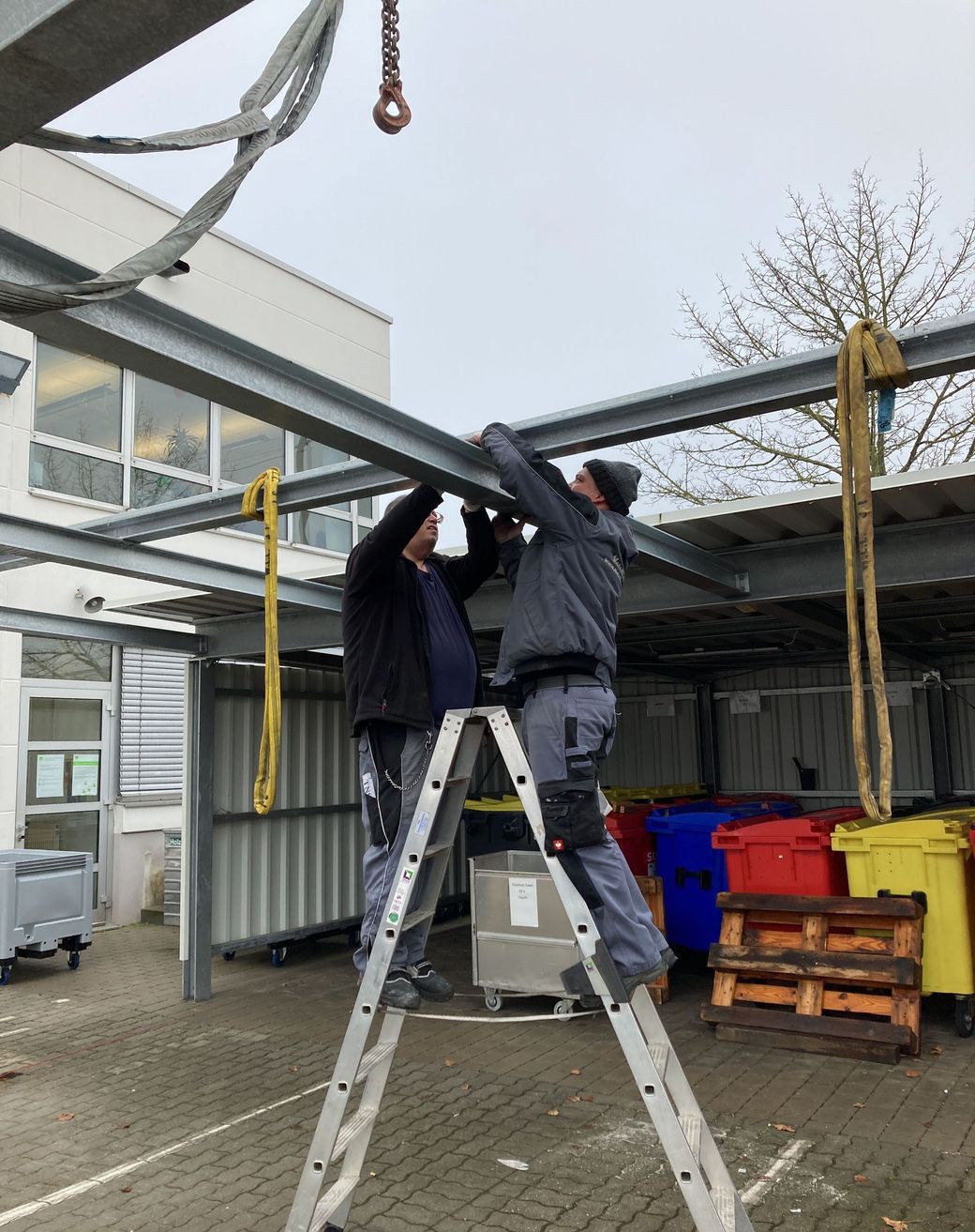 Zwei Metallbauer beim Aufbau eines Mülltonnenhauses aus Metall