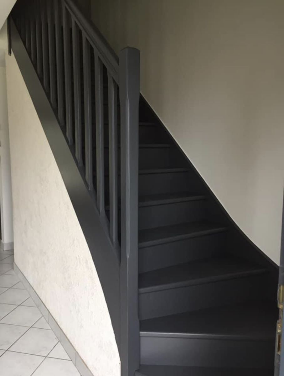 Un escalier aux rampes et marches gris foncé, adossé à un mur clair et au sol carrelé, dans l'entrée.