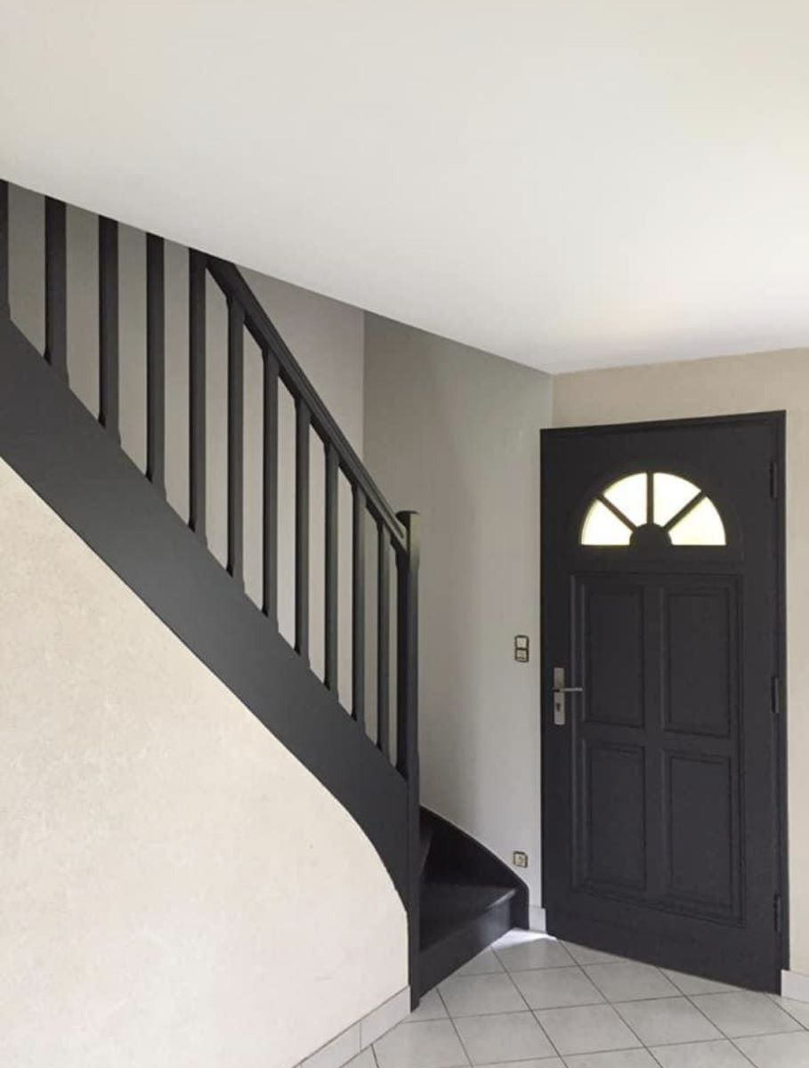 Un couloir avec un escalier gris foncé assorti à la porte d'entrée et des murs aux tons clairs et neutres.