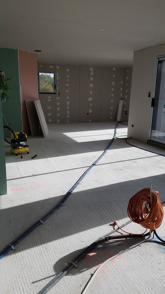 Une pièce intérieure en construction, avec des murs nus, un sol en béton, des outils et un câble électrique enroulé au sol.