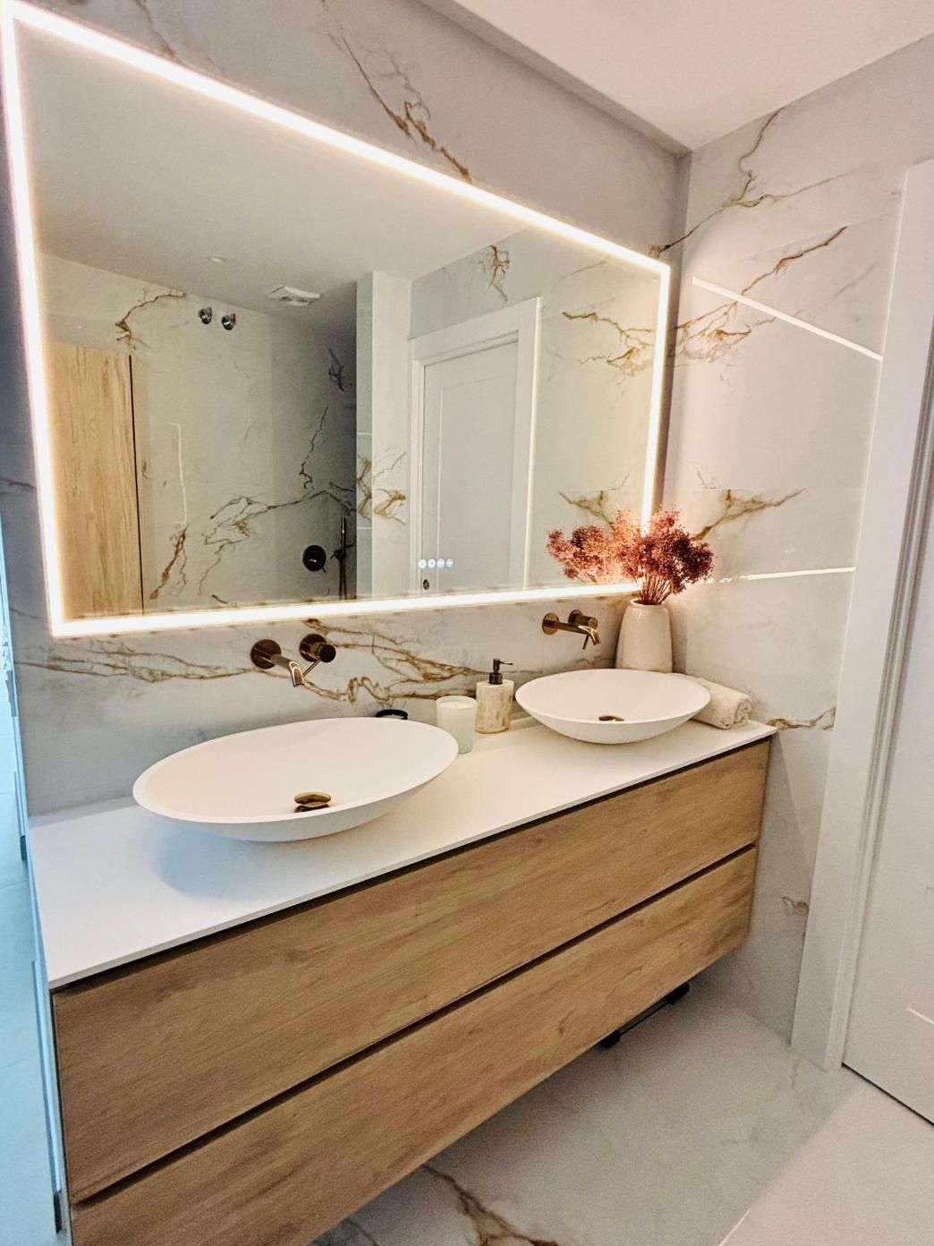 Tocador de baño moderno con cajones de madera, lavabos redondos sobre encimera, espejo de pared y azulejos de mármol