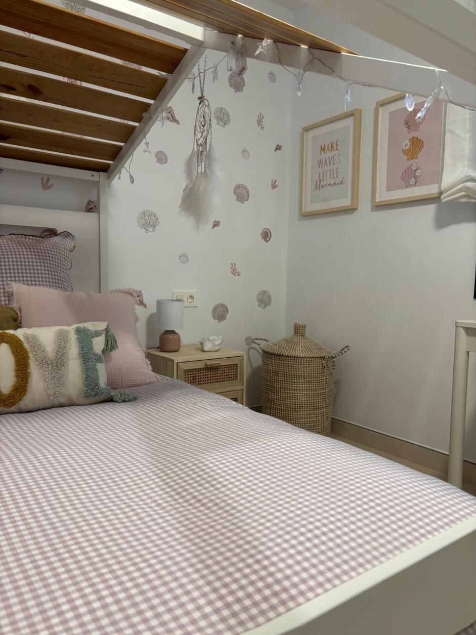 Acogedora habitación con una colcha de cuadros rosas, cojines en tonos pastel y cuadros enmarcados 