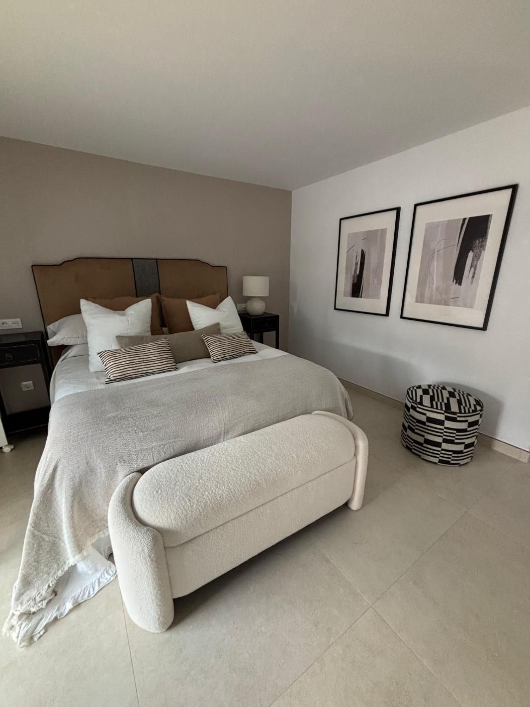 Habitación luminosa con una cama bien hecha, decoración neutra y cuadros enmarcados en la pared.