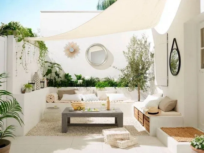 Sala de estar de patio de color blanco brillante con asientos modulares, mesa de centro, plantas y toldo parasol.
