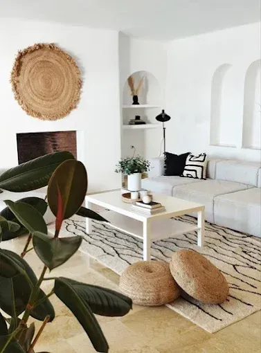 Sala de estar luminosa y minimalista con sofá blanco, mesa de centro, alfombra tejida y una gran planta en maceta.