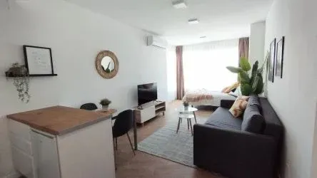 Luminoso salón moderno con sofá, televisor, mesa de comedor, plantas y gran ventanal.