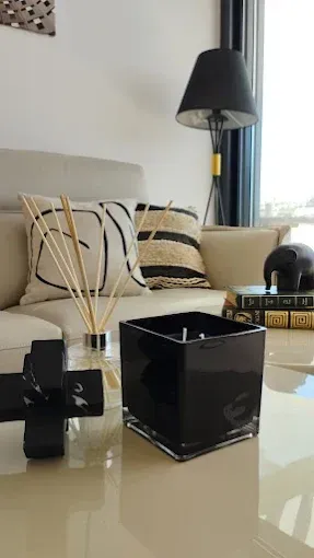 Sala de estar moderna con sofá beige, cojines a rayas, lámpara negra y mesa de centro de cristal con elementos decorativos.