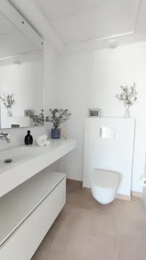 Baño minimalista blanco con tocador, espejo, decoración con jarrones e inodoro.