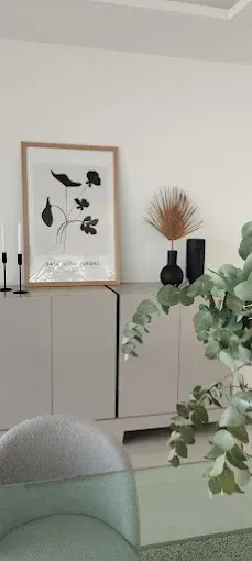 Sala de estar minimalista con cuadros enmarcados, jarrones negros y plantas sobre un mueble claro.