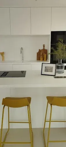 Cocina moderna blanca con taburetes amarillos, placa de cocina, fregadero y decoración de encimera.