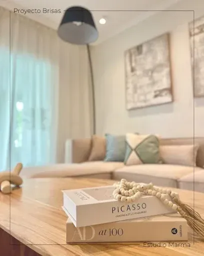Sala de estar moderna con sofá beige, mesa de centro de madera, lámpara y libro de Picasso en primer plano.