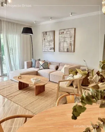 Luminoso salón con sofá beige, mesa de centro de madera, alfombra tejida y ventanas altas con cortinas transparentes.