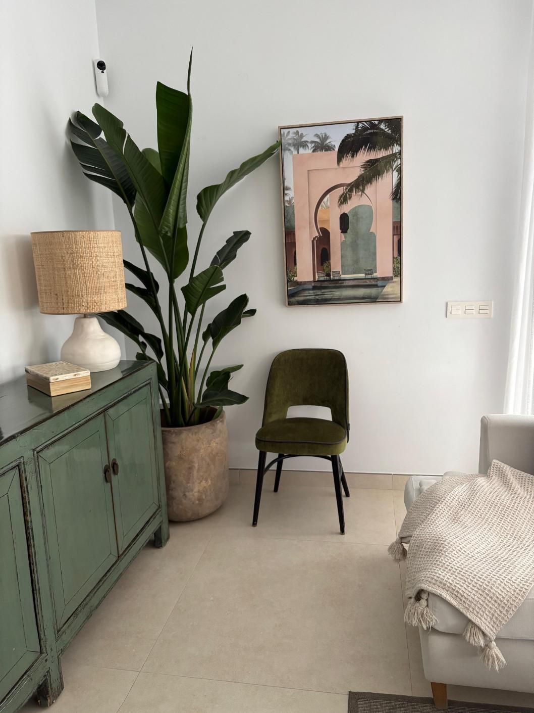 Rincón minimalista de salón con armario verde, planta en maceta, silla color oliva y cuadro abstracto en la pared.