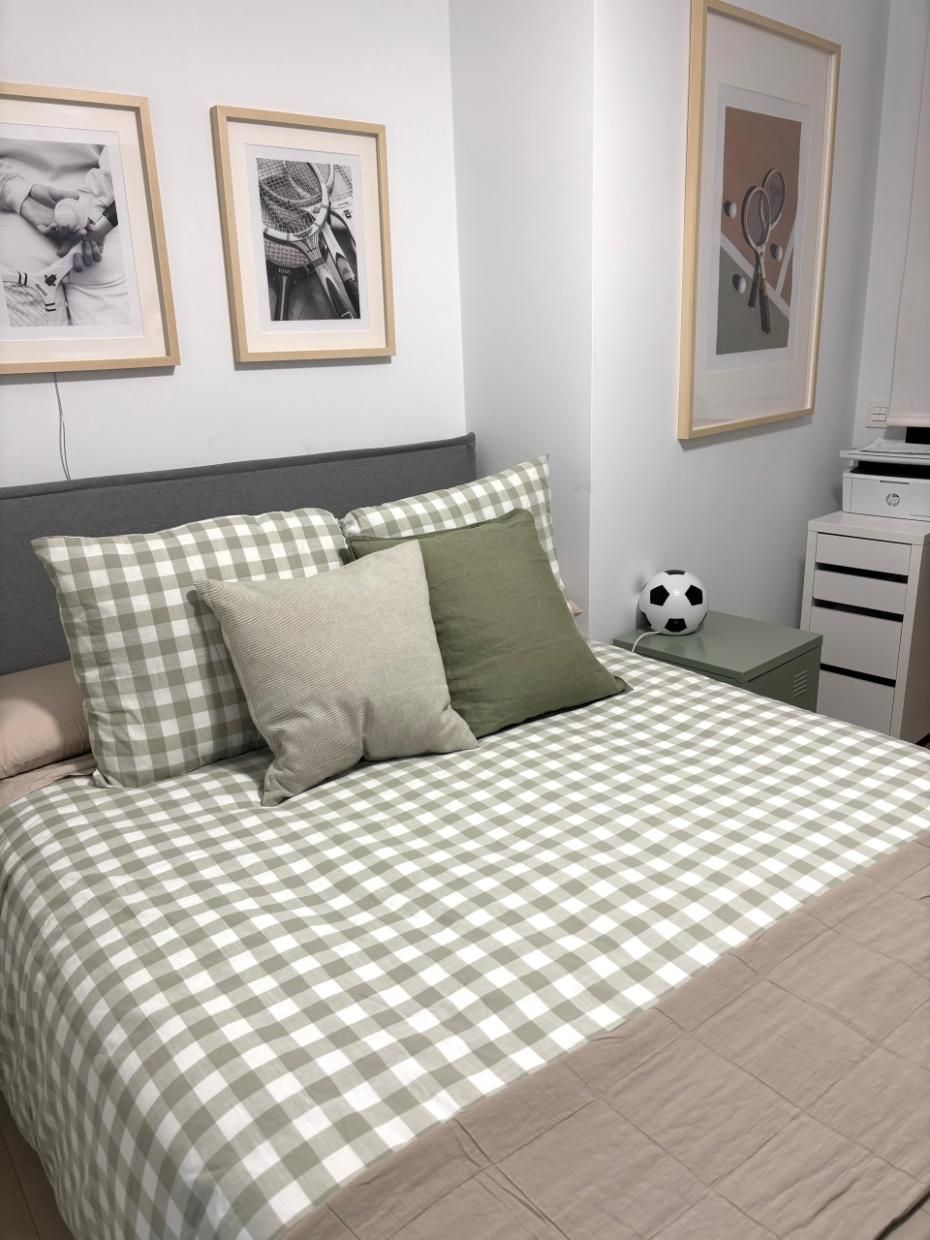Habitación ordenada con una colcha de cuadros verdes y blancos, almohadas, cuadros enmarcados 