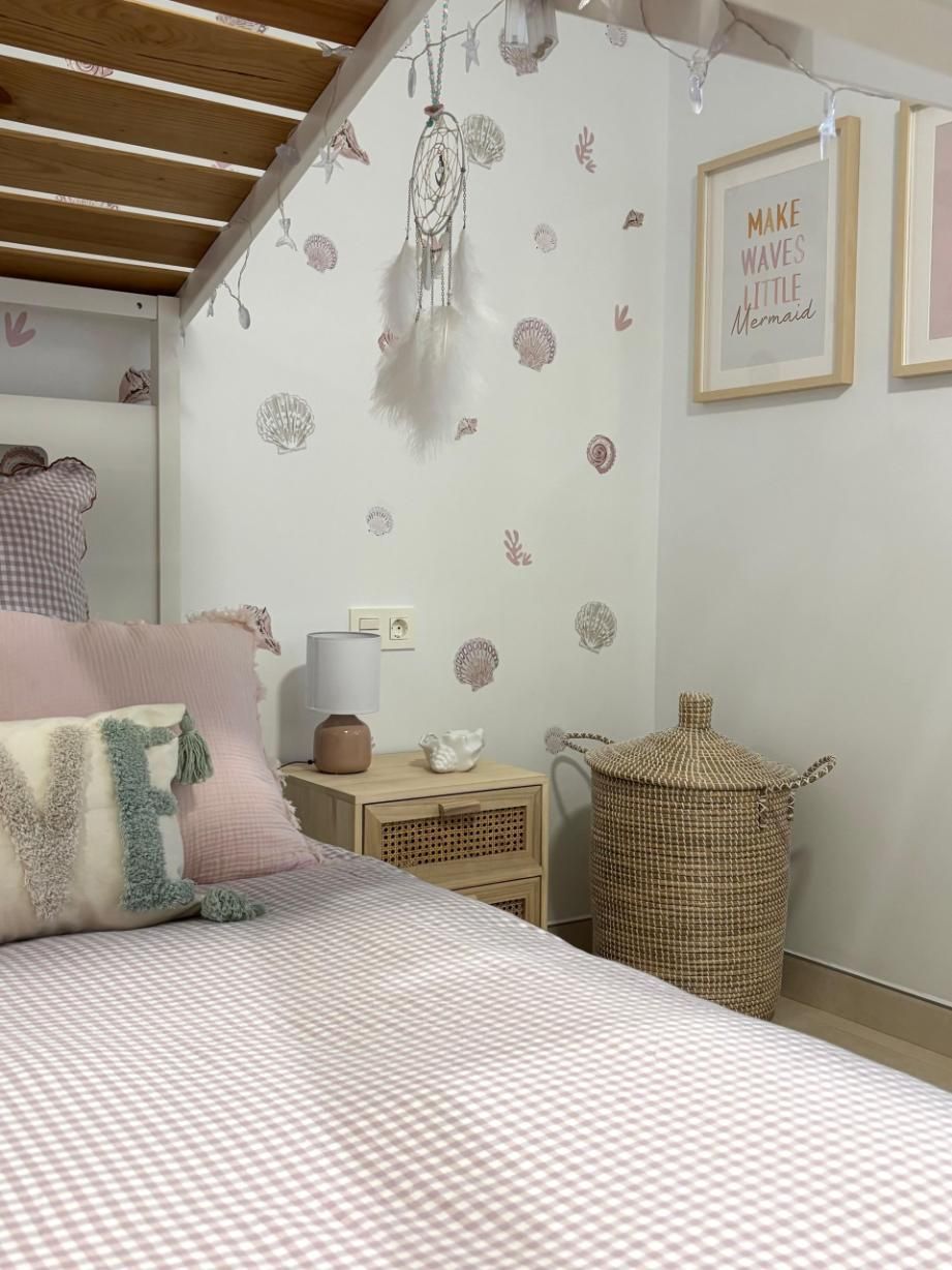 Acogedor dormitorio con cama de rayas rosas, mesita de noche de mimbre, decoración colgante y cuadros enmarcados.