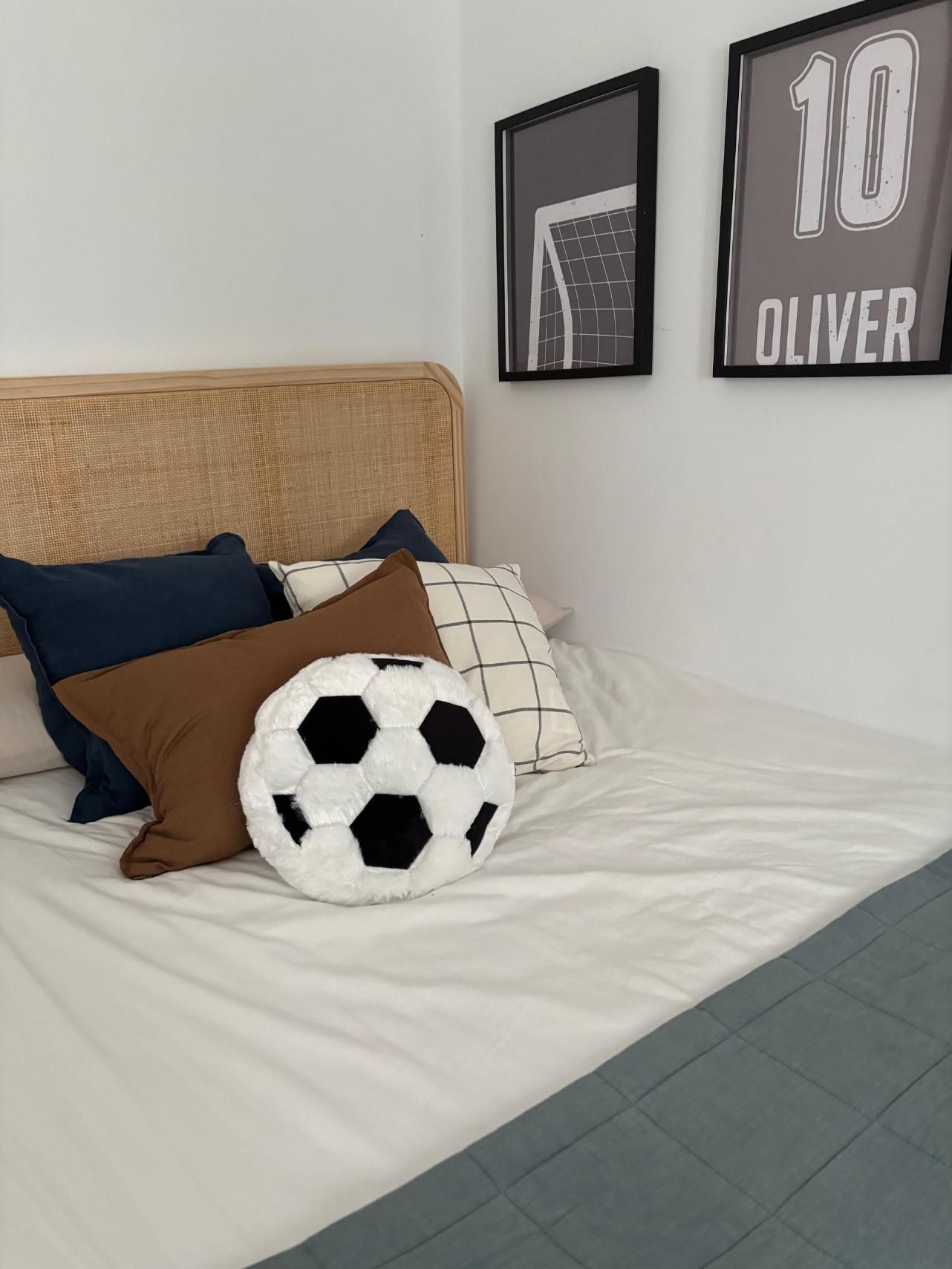 Cama blanca en una habitación con temática futbolística, decoración en blanco y negro y cuadros enmarcados en la pared.