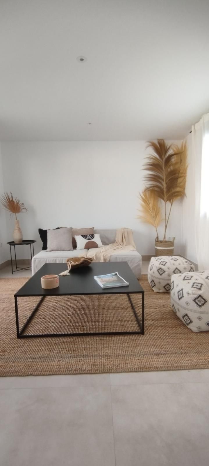 Sala de estar minimalista con un sofá blanco, una mesa de centro negra, una alfombra tejida y decoración 