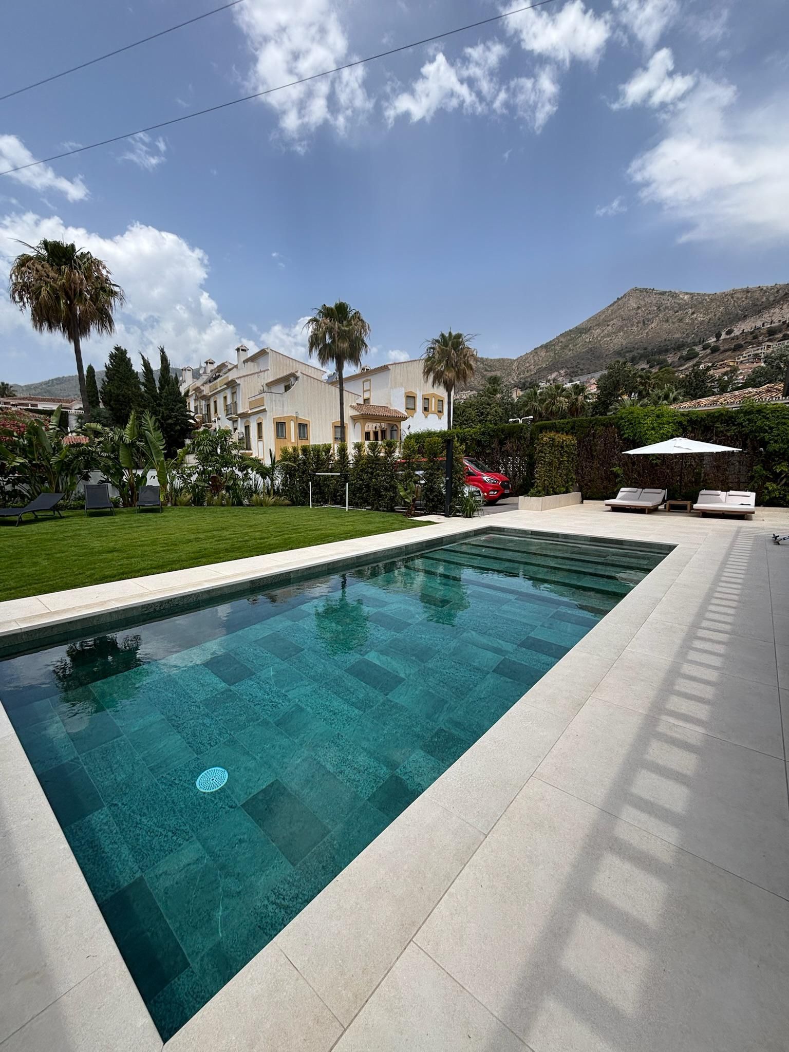 Sala de estar de patio de color blanco brillante con asientos modulares, mesa de centro, plantas y toldo parasol.