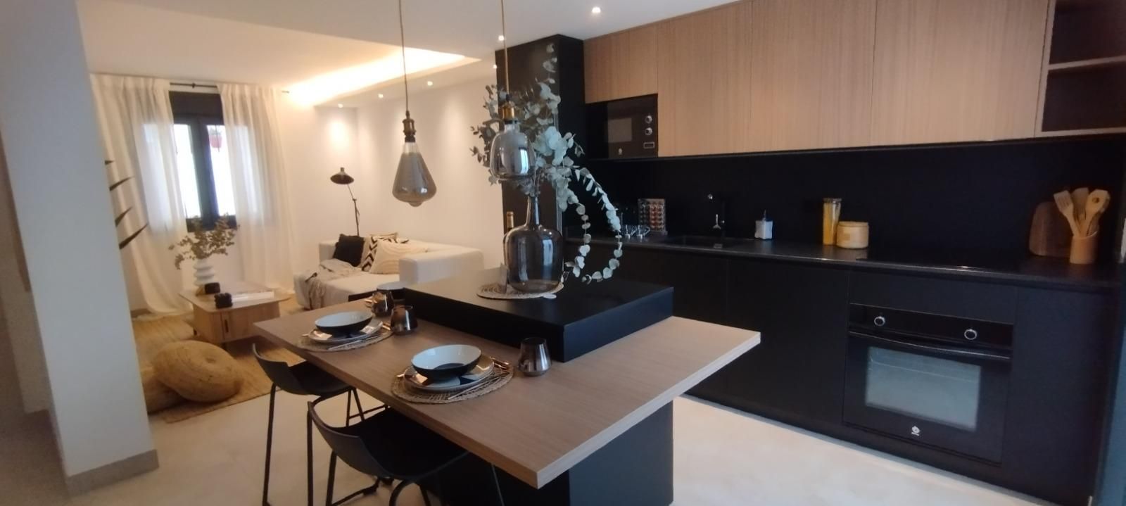 Cocina moderna con gabinetes oscuros, isla con asientos, lámparas colgantes y una estatua decorativa como pieza central.