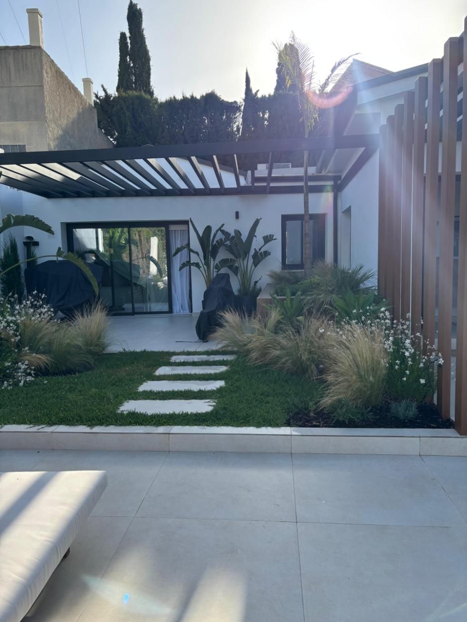 Casa blanca moderna con un pequeño jardín delantero paisajístico, escalones de piedra y una pérgola sobre el camino